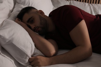 Photo of Sad man lying on bed at home