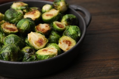Delicious roasted Brussels sprouts in baking dish on wooden table, closeup
