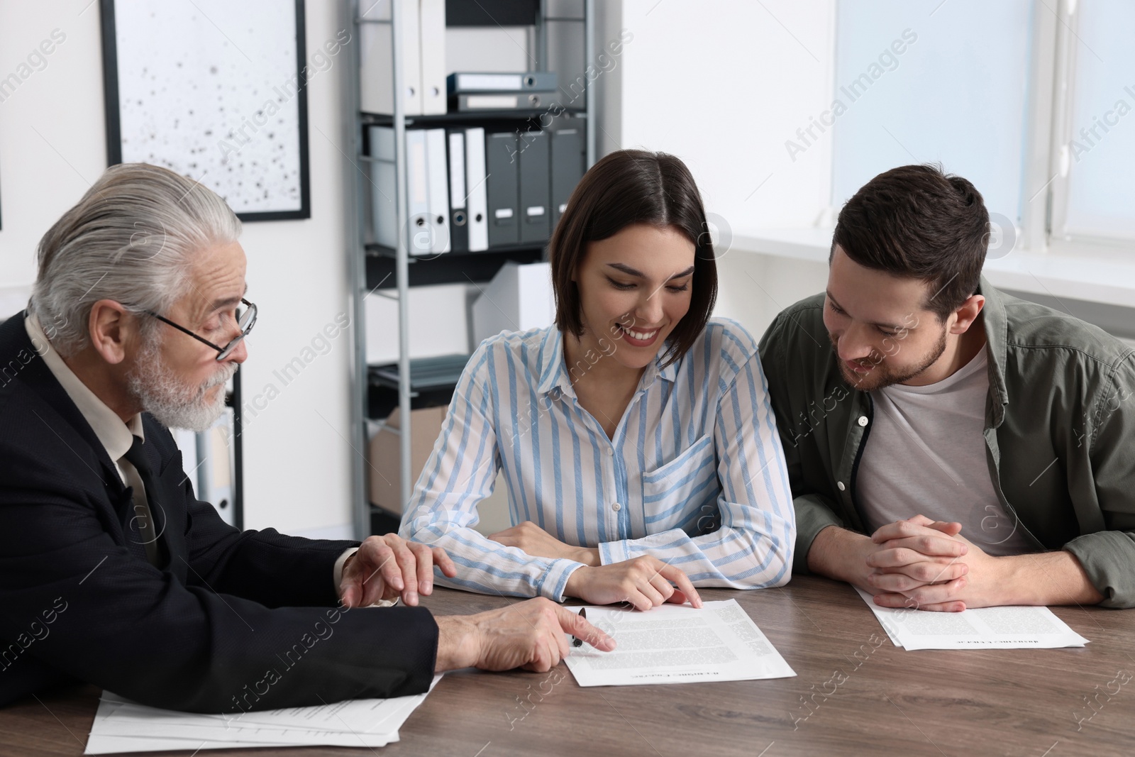 Photo of Young couple consulting insurance agent about pension plan at wooden table indoors