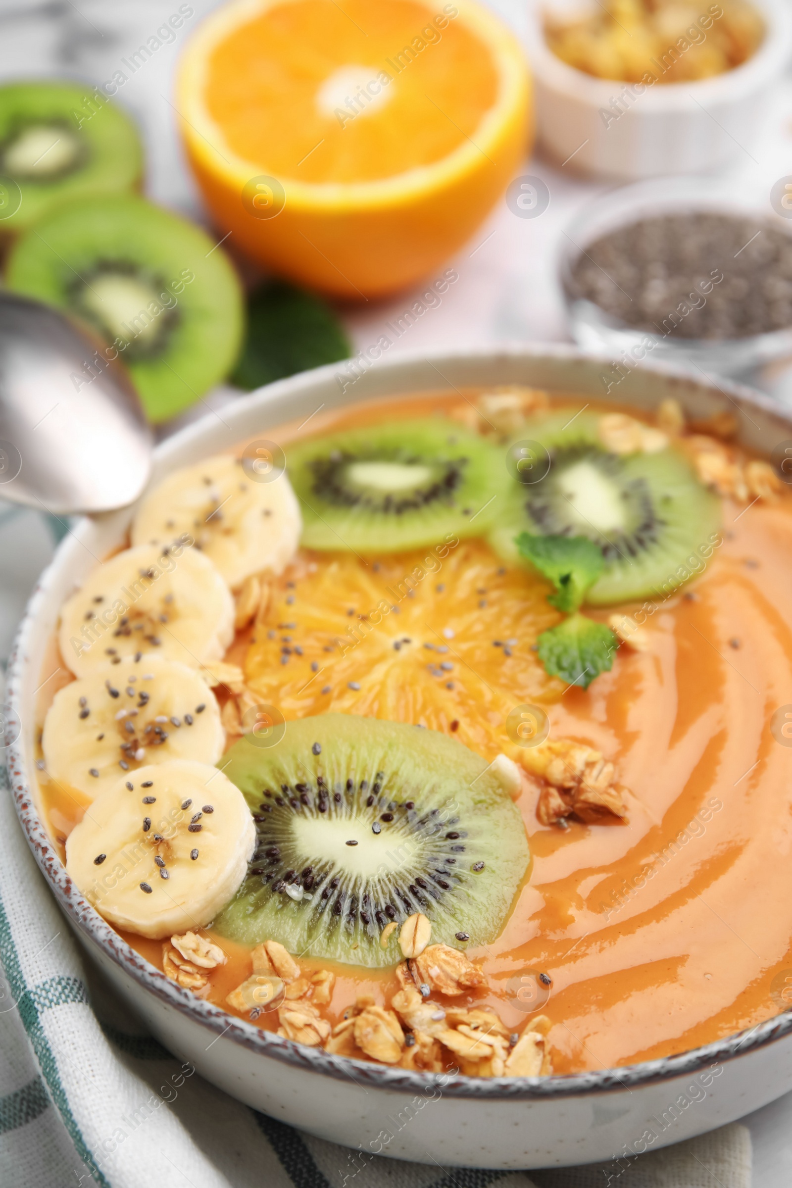 Photo of Bowl of delicious fruit smoothie with fresh banana, kiwi slices and granola served on white table, closeup