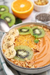 Bowl of delicious fruit smoothie with fresh banana, kiwi slices and granola served on white table, closeup