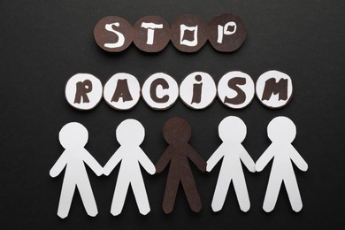Photo of Phrase Stop Racism near white and black paper people on dark background, flat lay