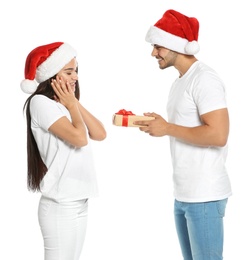 Young man giving gift box to girlfriend on white background. Happy couple celebrating Christmas