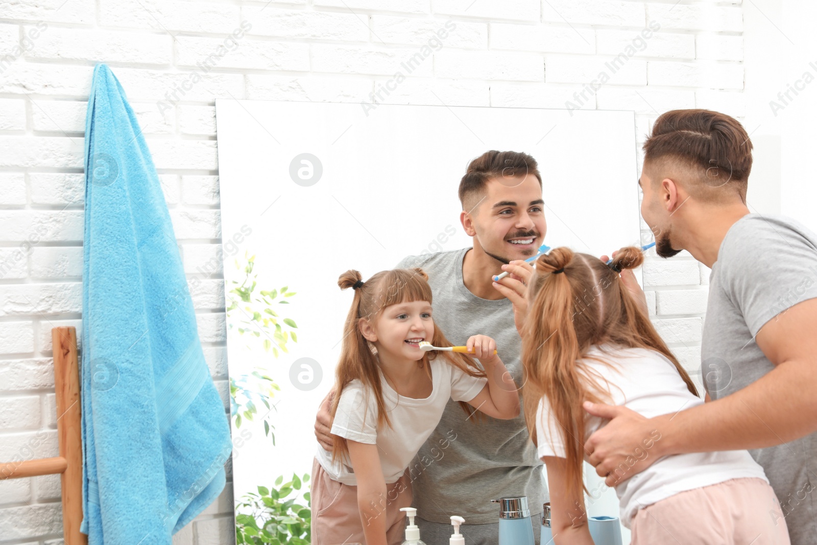 Photo of Little girl and her father brushing teeth together near mirror in bathroom at home. Space for text