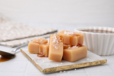 Photo of Delicious candies with sea salt and caramel sauce on white tiled table, closeup