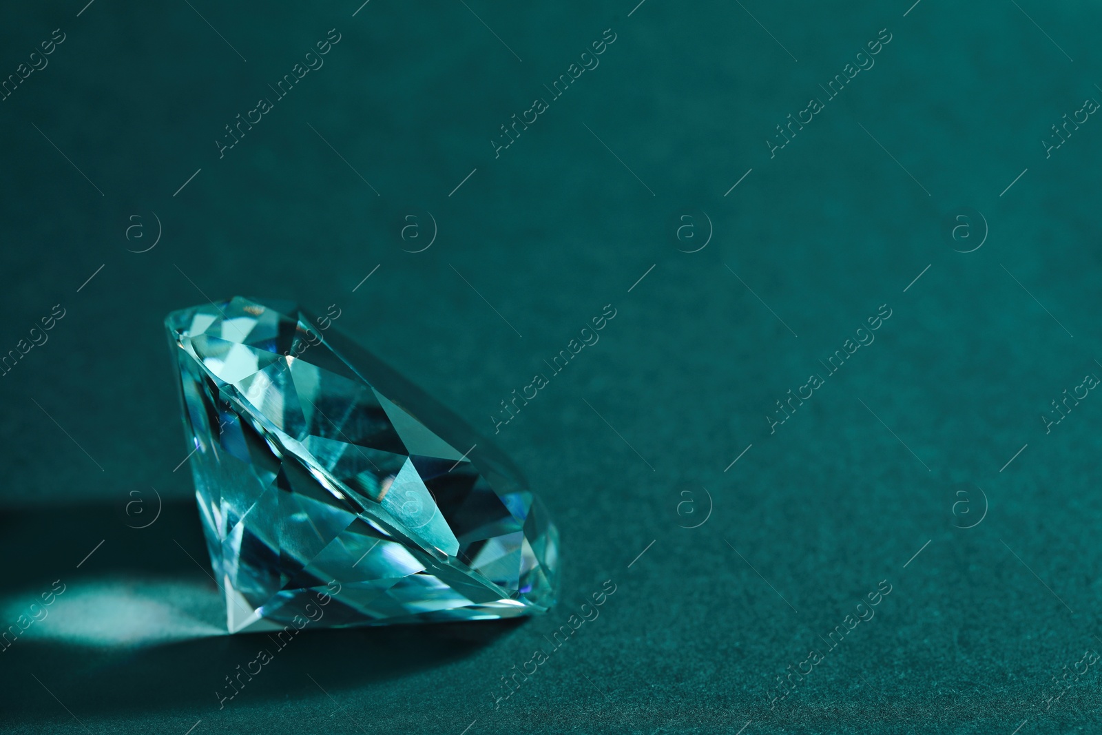 Photo of Beautiful dazzling diamond on green textured background, closeup. Space for text