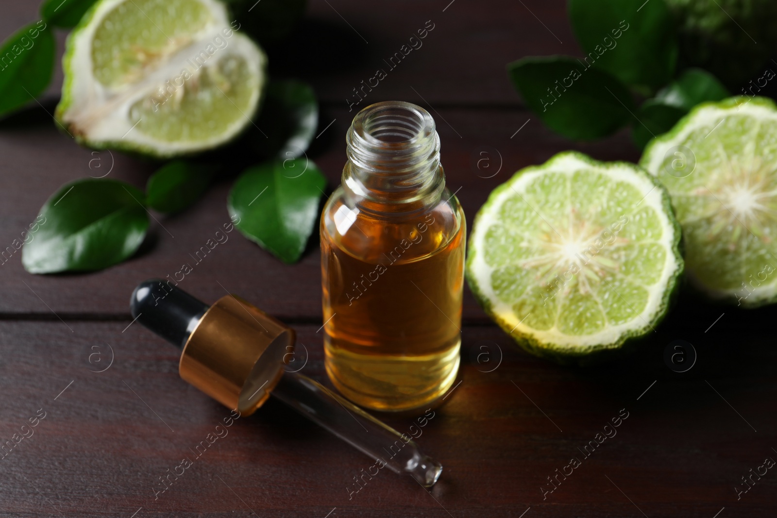 Photo of Bottle of essential oil, pipette and fresh bergamot fruits on wooden table