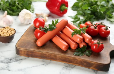 Photo of Fresh raw vegetarian sausages with parsley, tomatoes and soybeans on white marble table