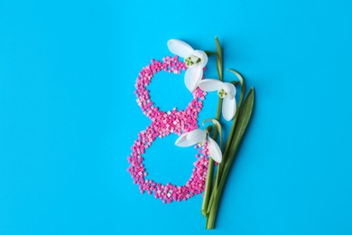 Beautiful snowdrops and number 8 made of decorative mosaic stones on light blue background, flat lay