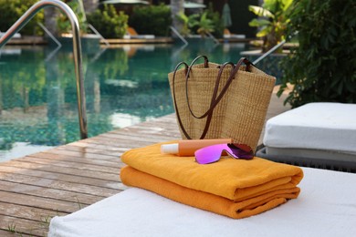 Photo of Wicker bag and beach accessories on sunbed near outdoor swimming pool. Luxury resort