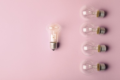 Photo of One different light bulb standing out from others on color background, top view