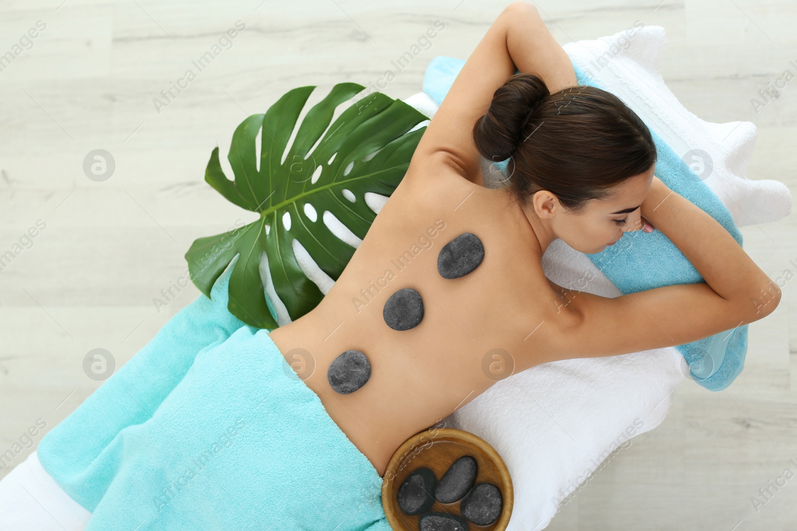 Photo of Beautiful young woman getting hot stone massage in spa salon, top view