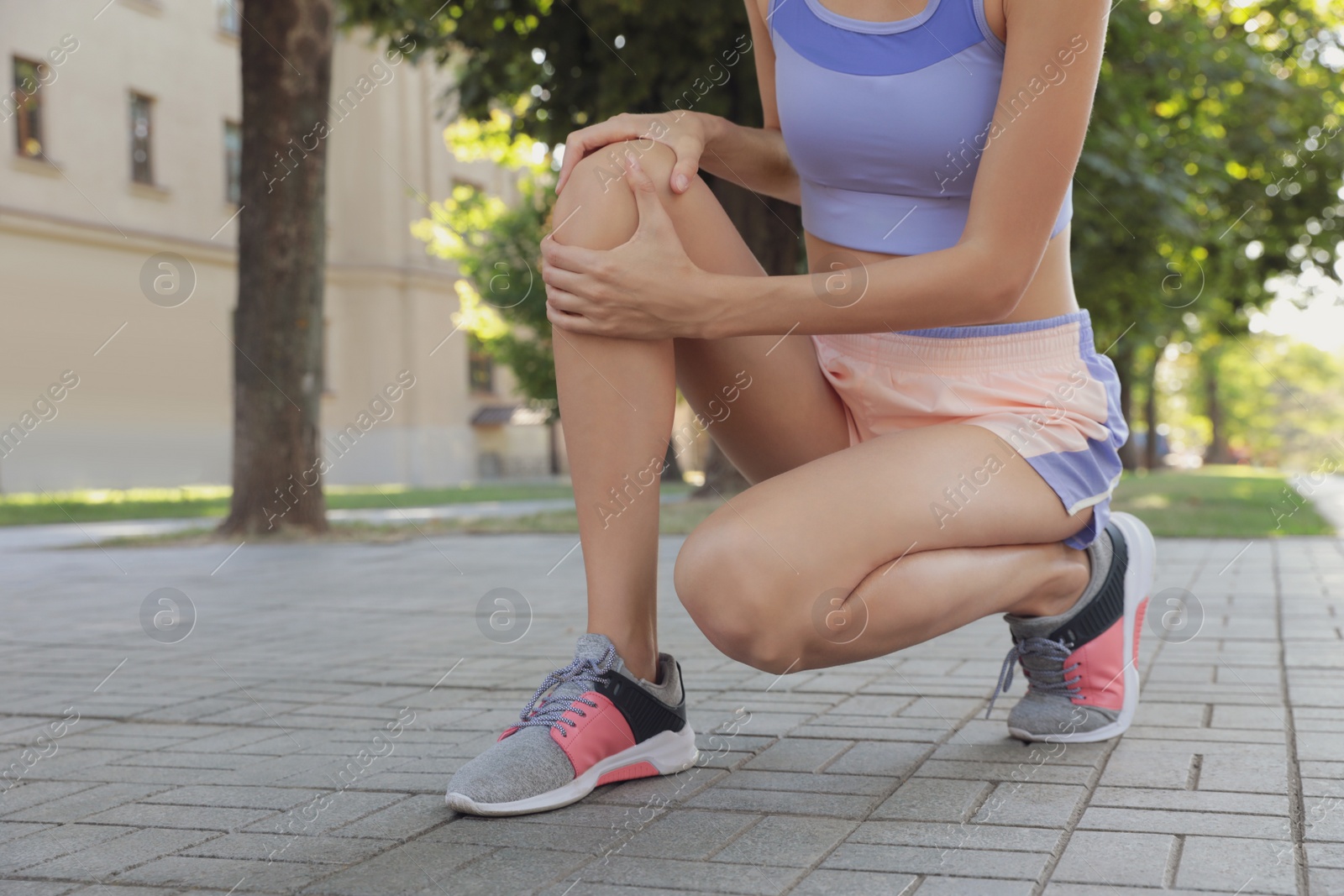 Photo of Young woman in sportswear having knee problems on city street, closeup