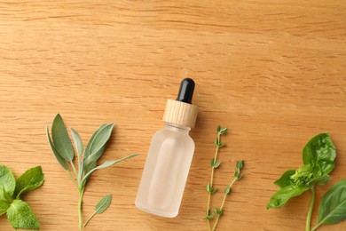 Bottle of essential oil and fresh herbs on wooden table, flat lay. Space for text