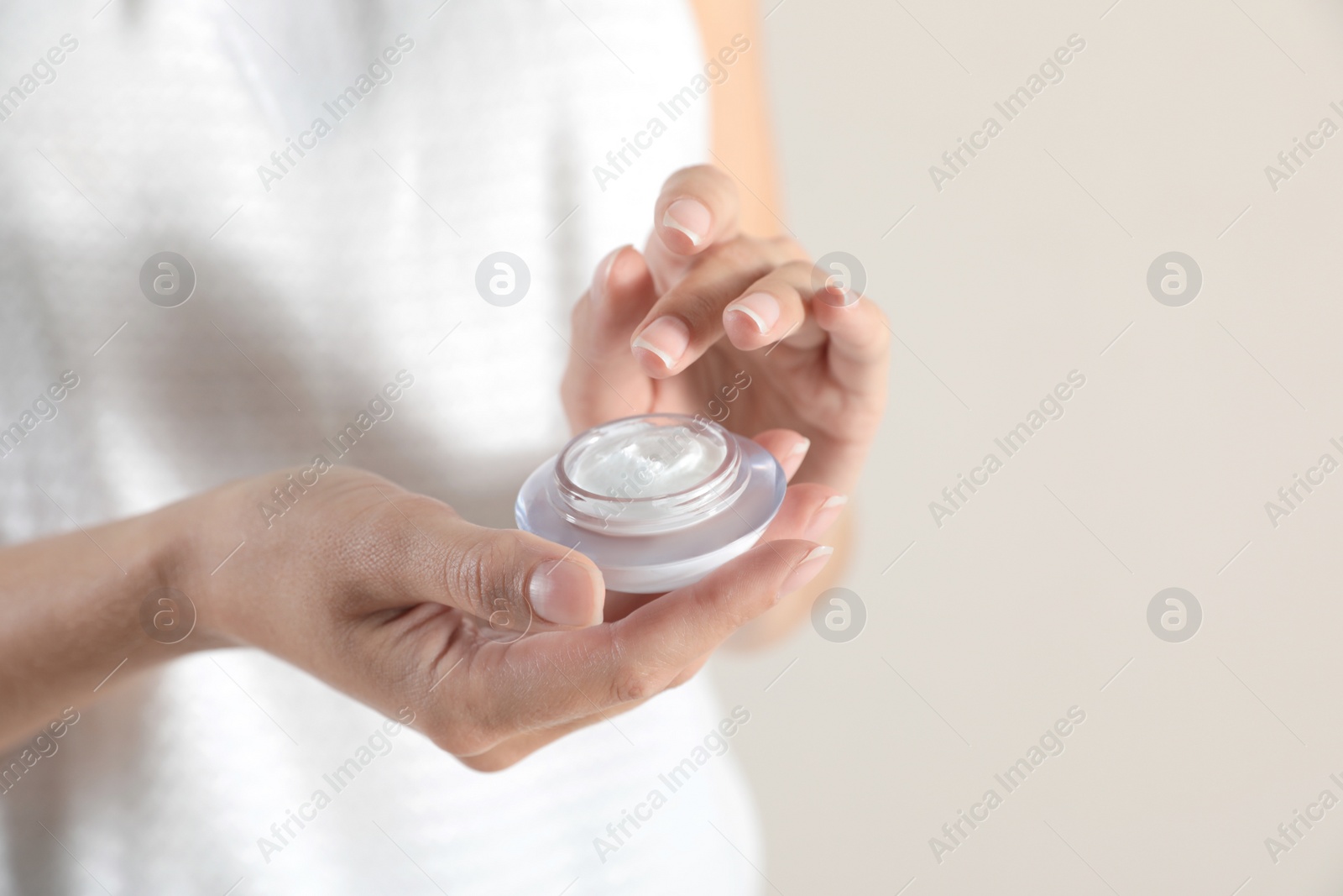 Photo of Young woman holding glass jar of cream on light background, closeup. Space for text