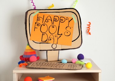 Photo of Fake computer with words Happy Fool's Day and party accessories on table