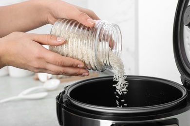 Photo of Woman pouring rice from jar into cooker in kitchen, closeup