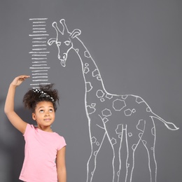 African-American child measuring height near chalk giraffe drawing on grey wall