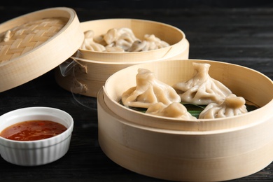 Bamboo steamers with tasty baozi dumplings and bowl of sauce on table