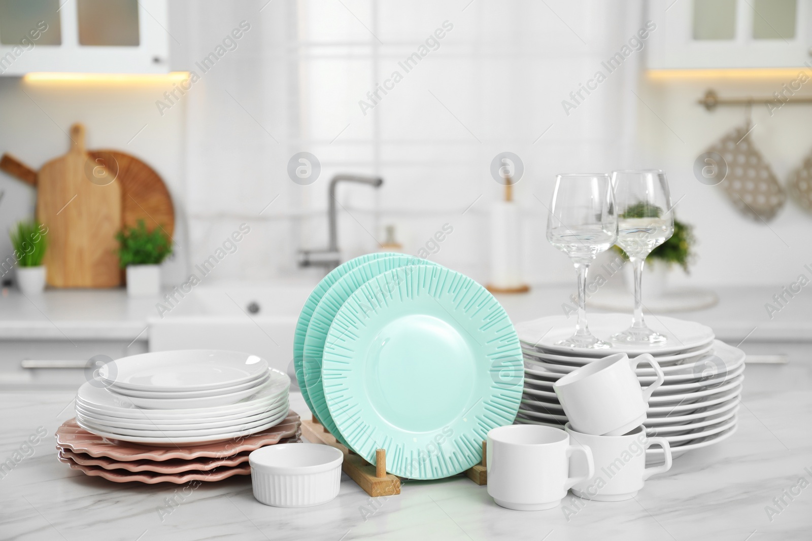 Photo of Clean plates, cups, glasses and bowl on white marble table in kitchen