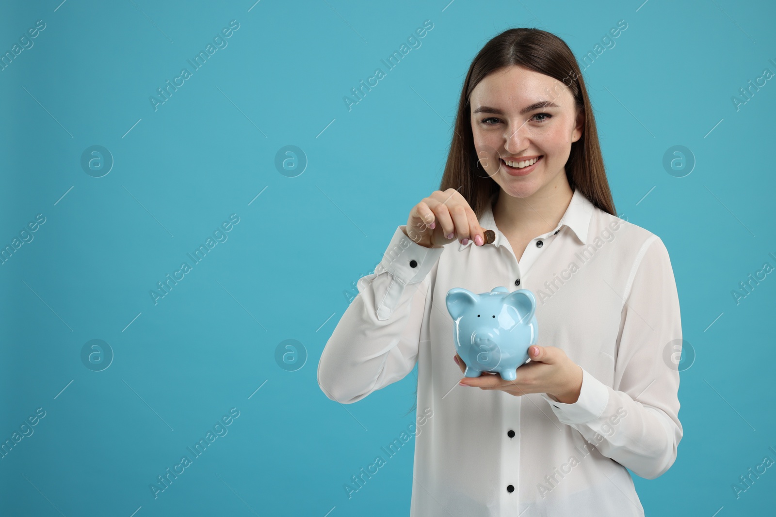 Photo of Happy woman putting coin into piggy bank on light blue background, space for text