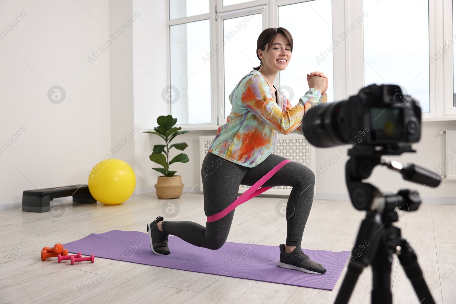 Photo of Happy sports blogger training with resistance band while recording fitness lesson at home