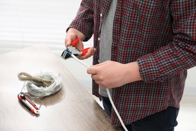 Photo of Professional electrician stripping wiring indoors, closeup view