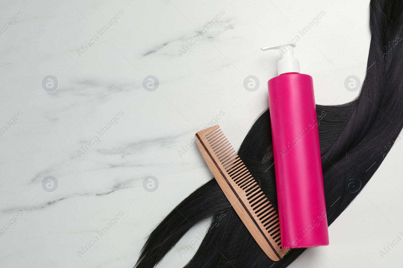 Photo of Spray bottle with thermal protection, lock of brunette hair and hairbrush on white marble table, flat lay. Space for text