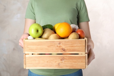 Photo of Woman holding wooden crate with fruits and vegetables on color background, closeup
