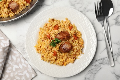 Tasty rice pilaf with meat served on marble table, flat lay