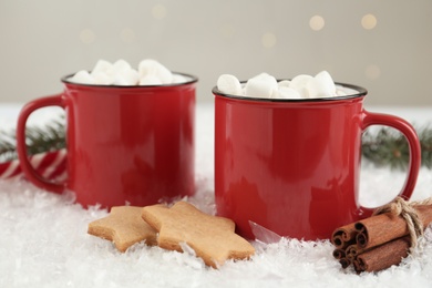Photo of Hot drinks with marshmallows in red cups, cookies and cinnamon on snow