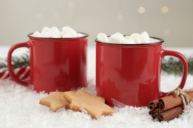 Hot drinks with marshmallows in red cups, cookies and cinnamon on snow