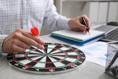 Business targeting concept. Man with dart aiming at dartboard at gray table indoors, closeup