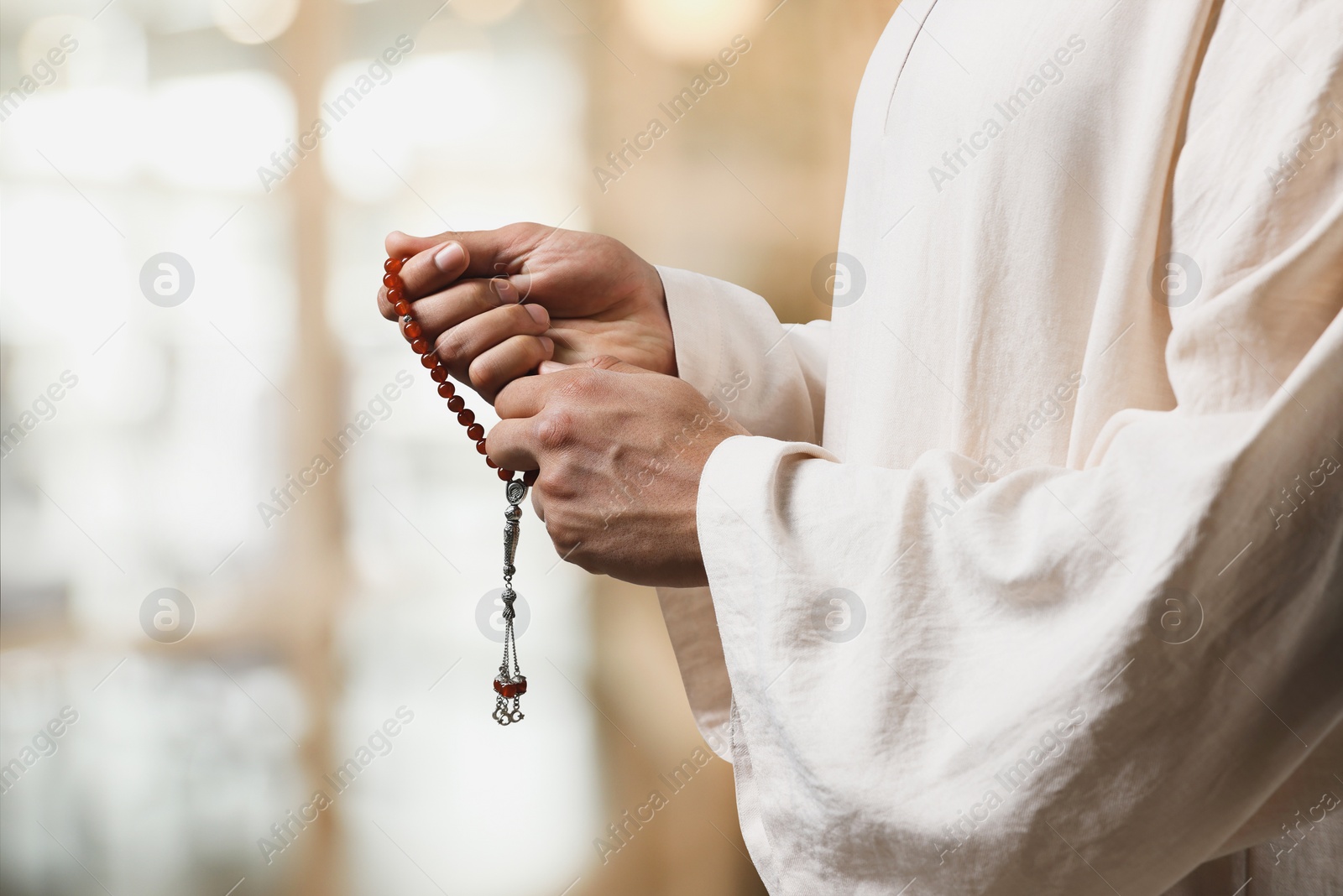 Image of Muslim man with misbaha praying on blurred background, closeup. Space for text