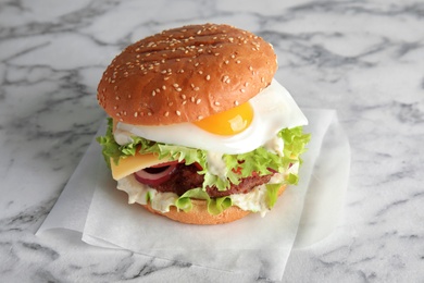 Photo of Tasty burger with fried egg on marble background