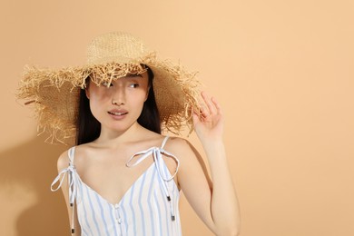 Photo of Beautiful young woman in straw hat on beige background, space for text