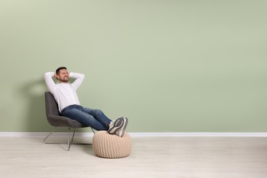 Photo of Happy man sitting in armchair near light green wall indoors, space for text