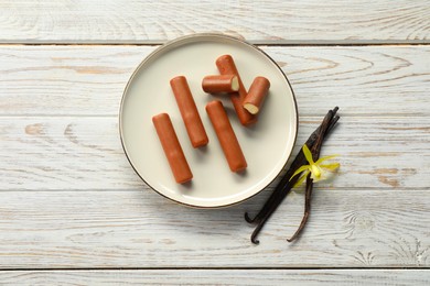 Photo of Glazed curd cheese bars, vanilla pods and flower on white wooden table, top view