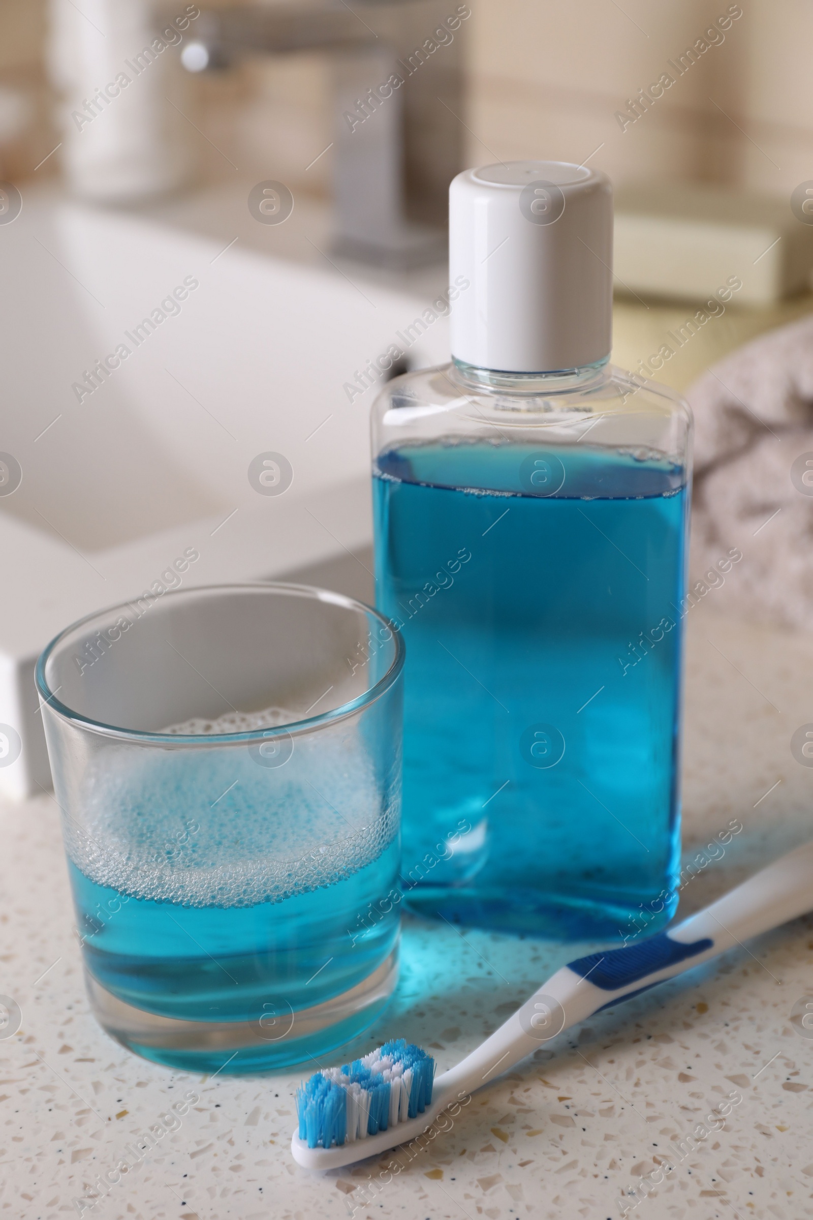 Photo of Fresh mouthwash in bottle, glass and dental floss on countertop, closeup