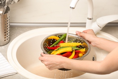 Photo of Woman washing chili peppers over sink, closeup
