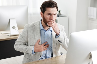 Photo of Sick man coughing at workplace in office. Cold symptoms