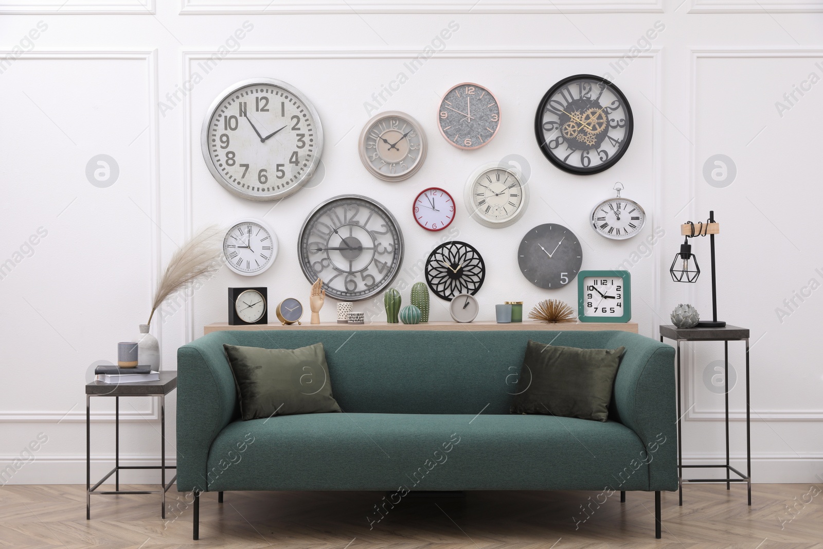 Photo of Collection of different clocks and comfortable sofa in stylish room. Interior design