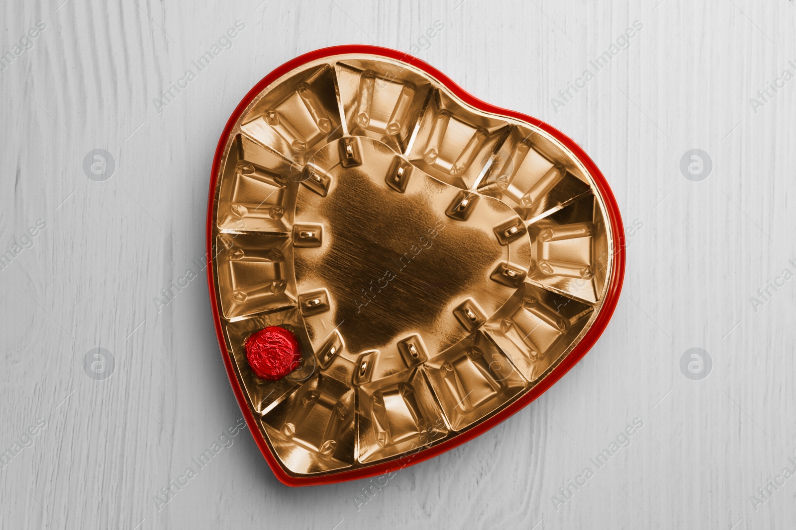 Photo of Partially empty box of chocolate candies on white wooden table, top view