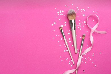 Photo of Different makeup brushes, ribbon and shiny confetti on pink background, flat lay. Space for text