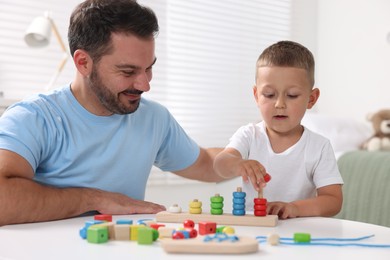 Photo of Motor skills development. Father and his son playing with stacking and counting game at table indoors