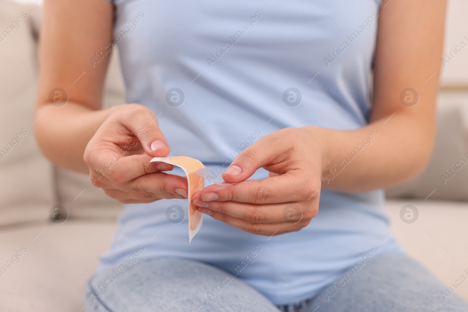 Photo of Woman opening sticking plaster on sofa, closeup