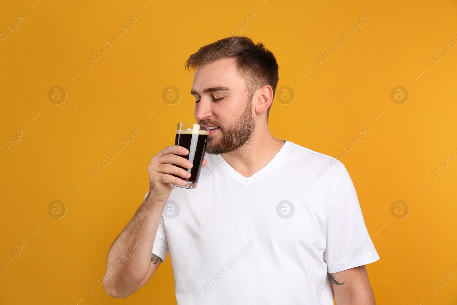 Photo of Handsome man with cold kvass on yellow background. Traditional Russian summer drink