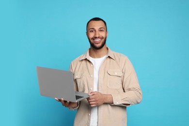 Photo of Smiling young man with laptop on light blue background