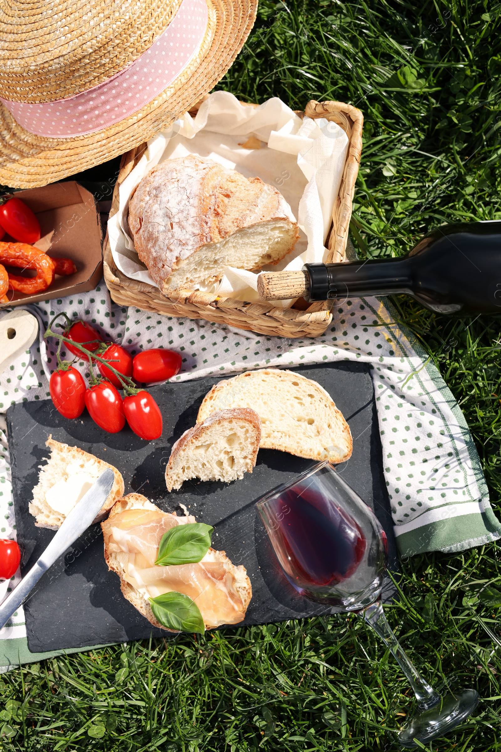 Photo of Blanket with wine and snacks for picnic on green grass, flat lay