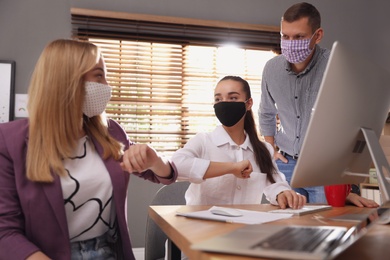 Photo of Coworkers with protective masks making elbow bump in office. Informal greeting during COVID-19 pandemic